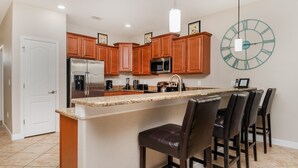 A kitchen with wooden cabinets, stainless steel appliances, a granite countertop, and a bar area with leather stools. - Wex1410 9 Bedroom Home (Davenport)