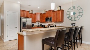 A kitchen with wooden cabinets, stainless steel appliances, a granite countertop, and a bar area with leather stools. - Wex1410 9 Bedroom Home (Davenport)