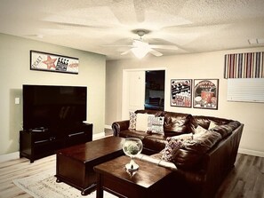 A living room with a flat-screen TV, a leather sofa, a coffee table, and a ceiling fan. - Wex1410 9 Bedroom Home (Davenport)