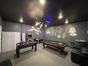 Een biljartruimte met een pooltafel, tafelvoetbaltafel en wanddecoratie.