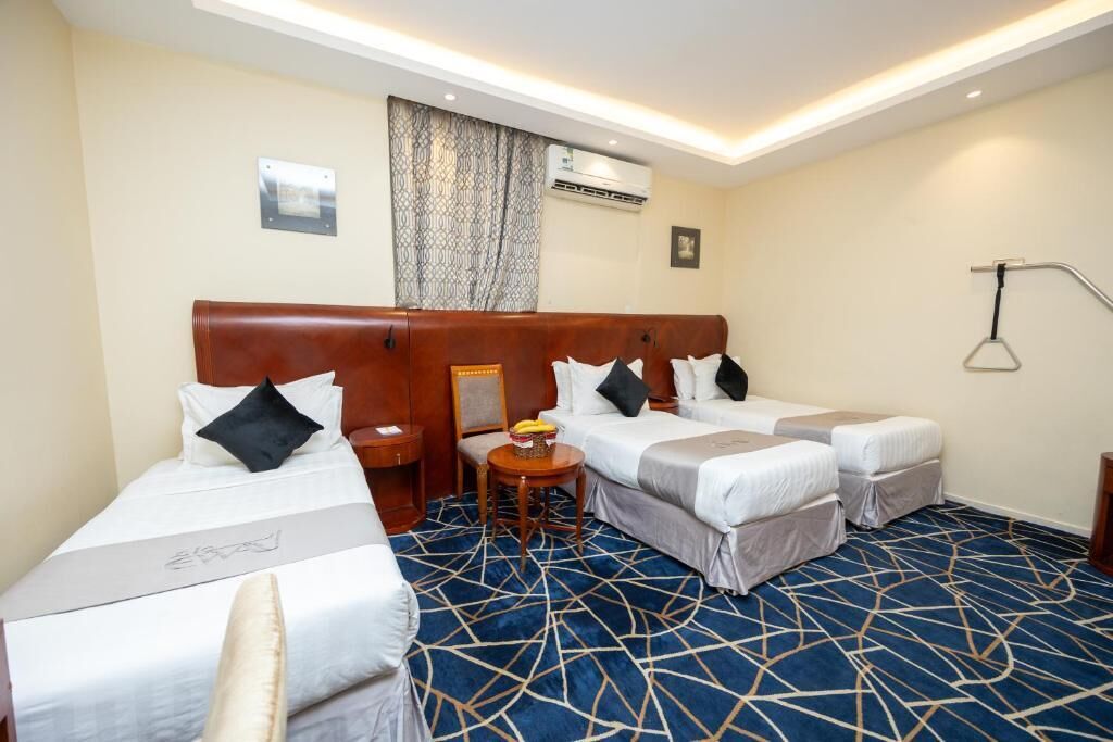 A hotel room with a large bed, two smaller beds, a desk, and a chair.