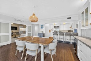 A modern kitchen with white cabinetry, a wooden dining table, and a hanging light fixture. - Residence 109 at The Grand (Wildwood)