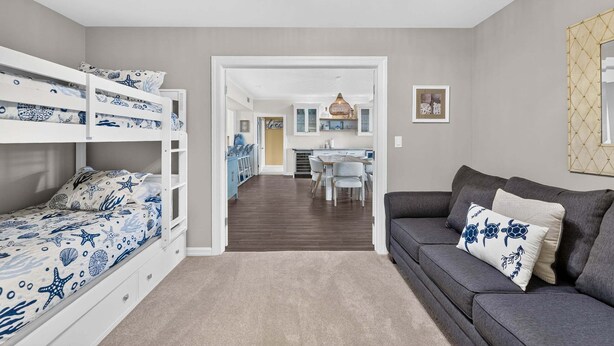 Ett rum med våningssängar, en grå soffa, en matplats och ett kök.