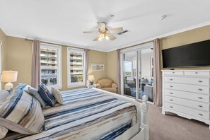 A hotel room with a bed, a TV, a ceiling fan, and a view of the outside balcony. - Residence 109 at The Grand (Wildwood)