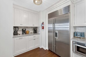 A kitchen with white cabinets, a stainless steel refrigerator, a coffee maker, a toaster, and a fire extinguisher. - Residence 109 at The Grand (Wildwood)