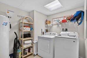 A laundry room with a washing machine, dryer, and a wooden shelf with folded clothes. - Residence 109 at The Grand (Wildwood)