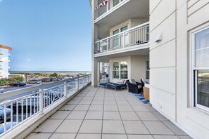 A balcony with a view of the sea, a parking area, and a building with multiple floors and balconies. - Residence 109 at The Grand (Wildwood)
