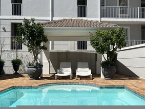 Ein Poolbereich mit zwei Liegestühlen unter einer Pergola, umgeben von Topfpflanzen.