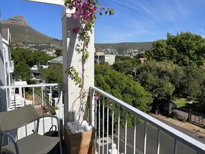 Ein Balkon mit Blick auf eine Stadtlandschaft, eine weiße Säule und eine Pflanze mit rosa Blüten.