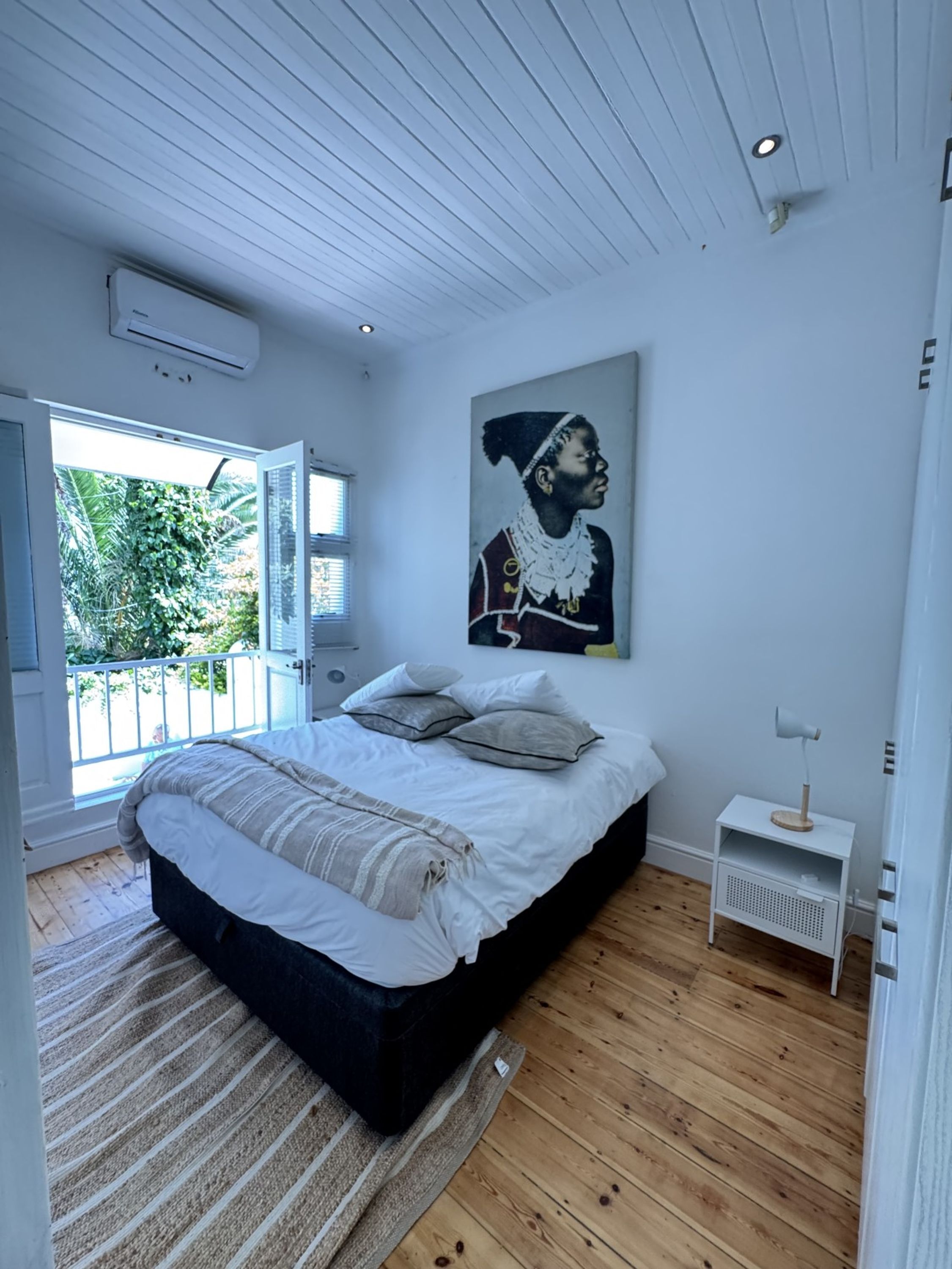 Een slaapkamer met een groot bed, een nachtkastje, een plafondventilator en een raam met uitzicht op groen.