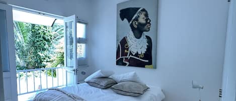 A bedroom with a large bed, a nightstand, a ceiling fan, and a window with a view of greenery.