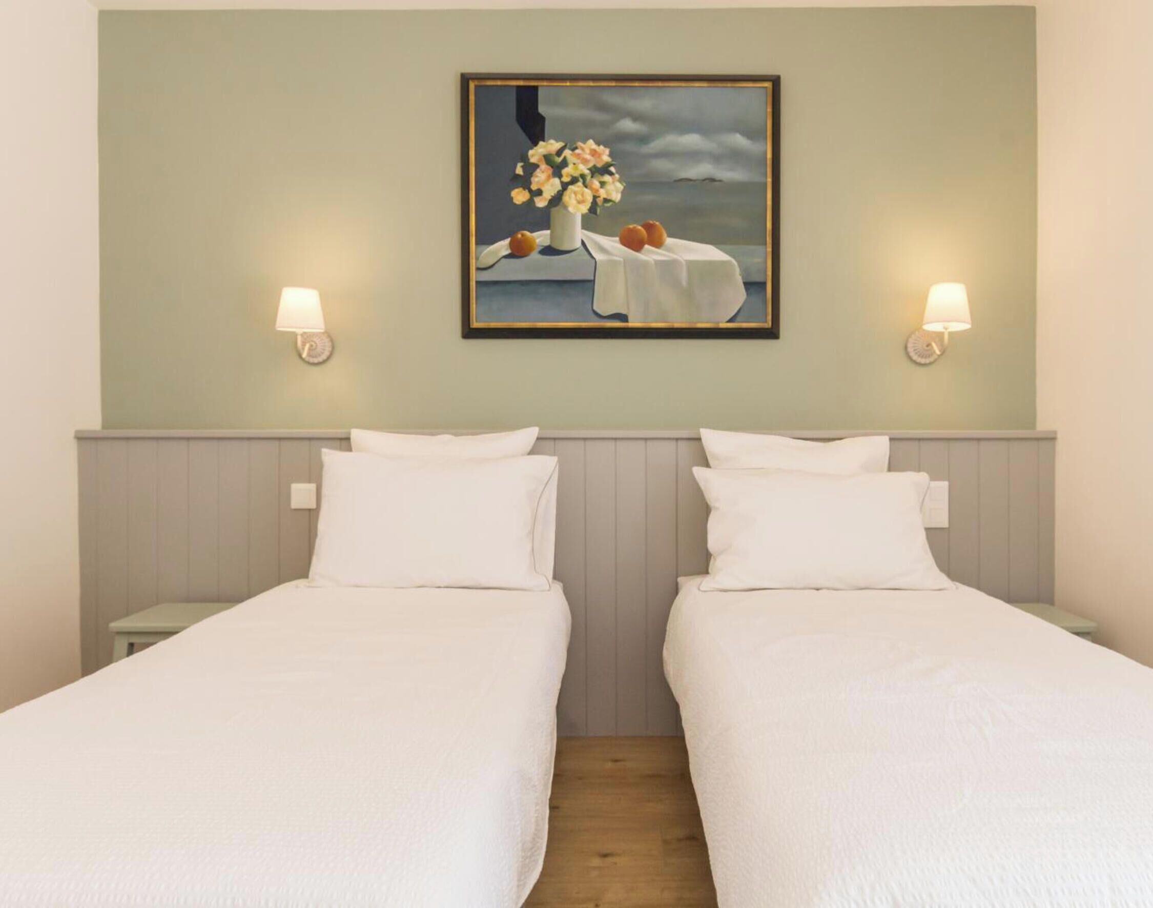 Une chambre d’hôtel avec deux lits, un tableau au mur et deux lampes fixées au mur.
