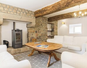A cozy room with a stone wall, a fireplace, a round wooden table, and a white sofa. - House with parking, pets welcome - 7 guests (Le Val-Saint-Père)