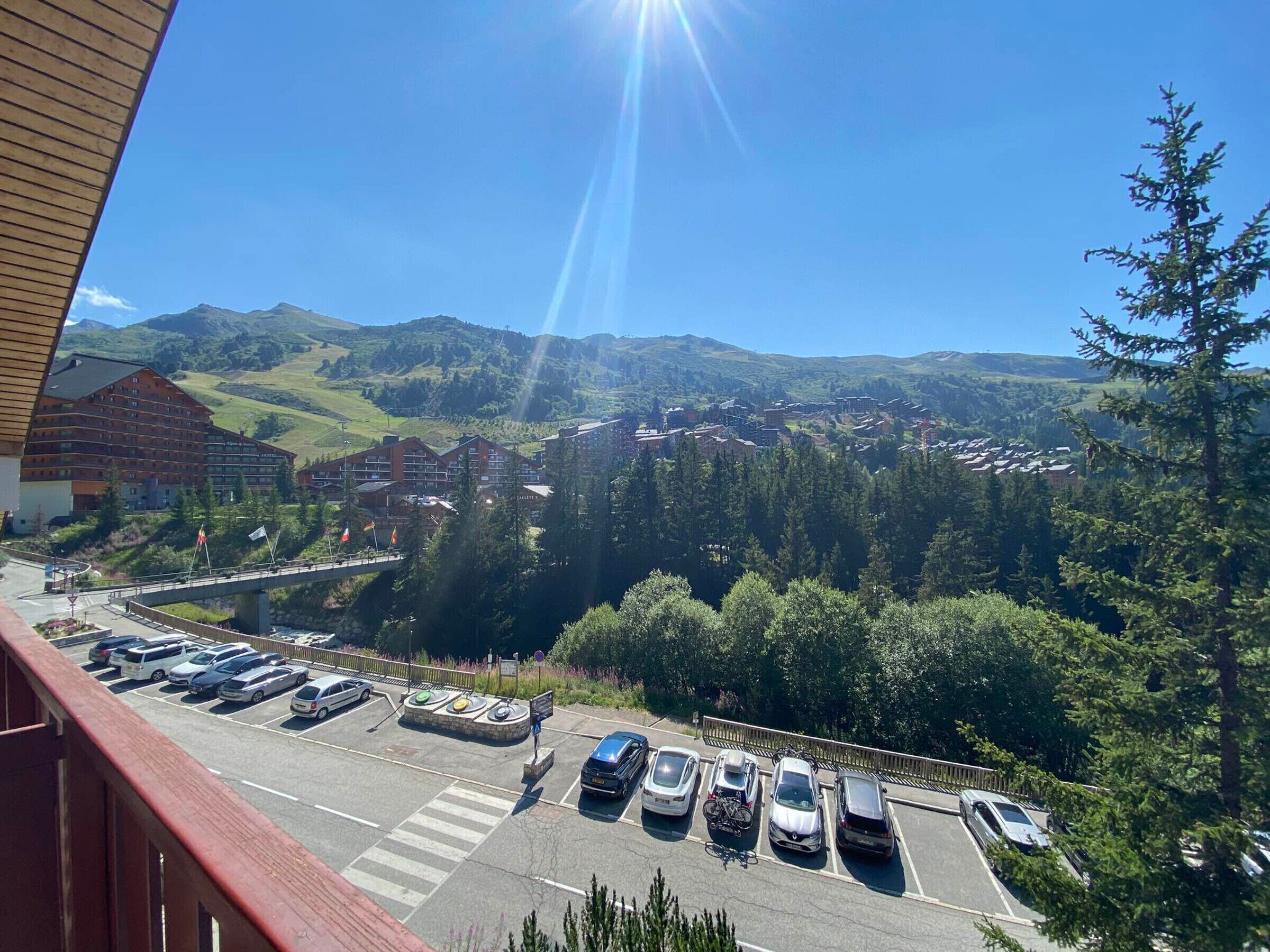 Ein Parkplatz mit Autos und einer Fußgängerüberweg, mit Blick auf eine gebirgige Landschaft mit Gebäuden und einer Brücke.