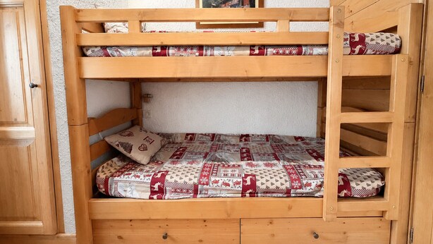 En køjeseng med træramme, nederste køje med et mønstret madras og en gavl med et billede.