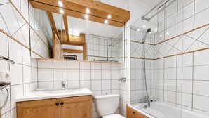 Et moderne badeværelse med en trækommode, toilet og badekar med glasvægge.