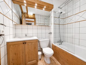 Ein modernes Badezimmer mit einem Holzlaufschrank, einer Toilette und einer Badewanne mit Glasabtrennung.