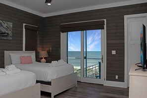 Un dormitorio con cama, mesita de noche, lámpara y vista al océano a través de un ventanal.