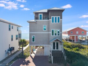 Un edificio de varios pisos con un balcón en el piso superior, una entrada principal con escalones y vista a la playa.