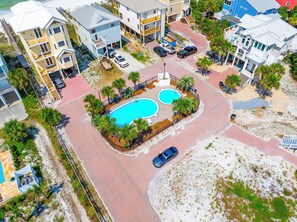 An aerial view of a residential area with two swimming pools, a paved road, and surrounding buildings. - 🌊Singing Waves | Stunning Beachfront | Community Pool | Pet Friendly (Cape San Blas)
