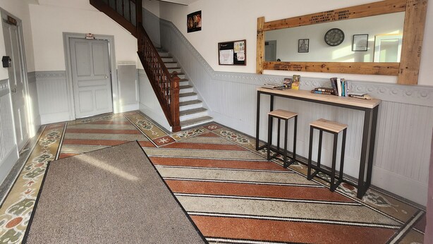 A hallway with a wooden staircase, a reception desk, and a wall-mounted mirror. - Charming apartment in city center - 2 guests (Luxeuil-les-Bains)