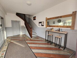 A hallway with a wooden staircase, a reception desk, and a wall-mounted mirror. - Charming apartment in city center - 2 guests (Luxeuil-les-Bains)