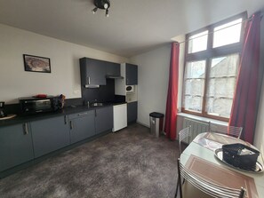 A compact kitchen with a toaster, sink, and cabinets. There's a window with curtains and a radiator. - Charming apartment in city center - 2 guests (Luxeuil-les-Bains)