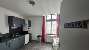 A compact kitchen with dark cabinets, a sink, and a window with red curtains. - Charming apartment in city center - 2 guests (Luxeuil-les-Bains)