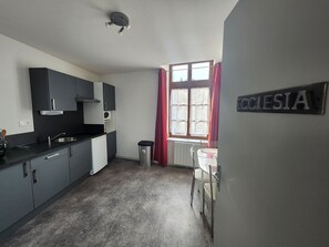 Eine kleine Küche mit dunklen Schränken, einem Spülbecken und einem Fenster mit roten Vorhängen.