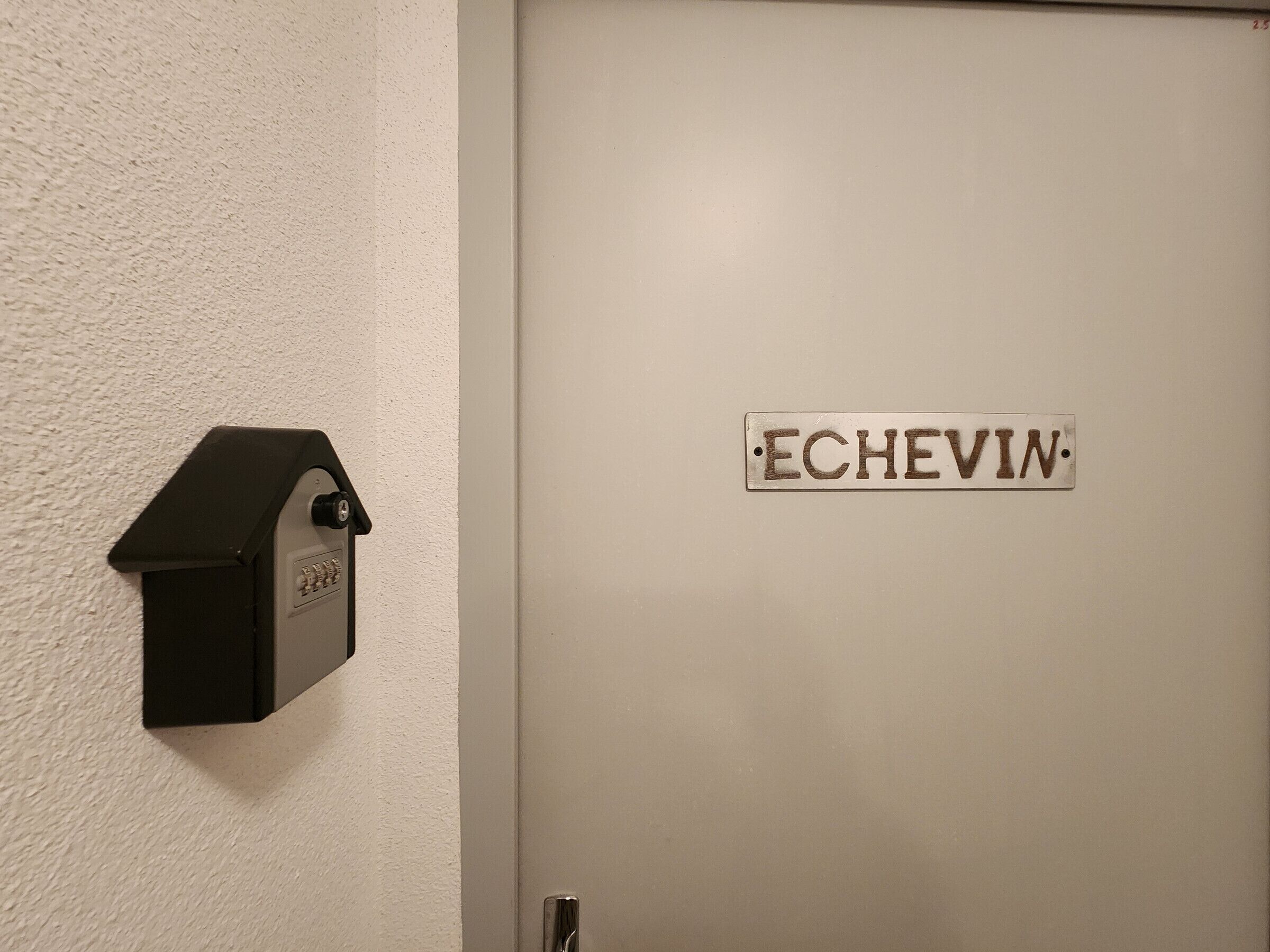 Eine Tür mit einem Schild, auf dem 'ECHEVIN' steht, und einem an der Wand befestigten Briefkasten.