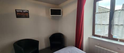 A hotel room with a bed, a desk, a chair, a TV, and a window with curtains.