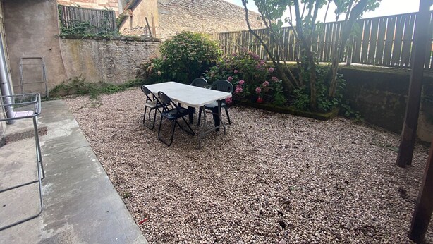 Un espace patio aménagé avec une table et des chaises, entouré de gravier, d’une clôture en bois et d’un mur en pierre.
