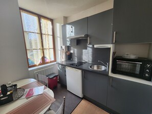 Eine kleine Küche mit Spüle, Herd, Mikrowelle und einem Fenster mit Vorhängen.
