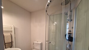Une salle de bain équipée de toilettes, d’un lavabo et d’une douche fermée par une paroi de verre.