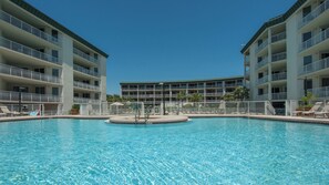 A swimming pool surrounded by a fence, with a multi-story building in the background. - 2BR Gulf-Front | Pool, Hot Tub & Direct Beach Access + Attraction Tickets! (Santa Rosa Beach)