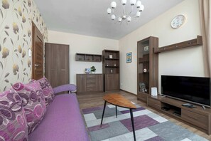 Ein modernes Wohnzimmer mit einer Couch, Fernseher, Holzschränken und einem Kronleuchter.