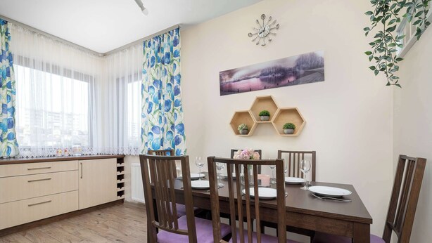 Un comedor con una mesa de madera, cuatro sillas y una ventana con cortinas ligeras.