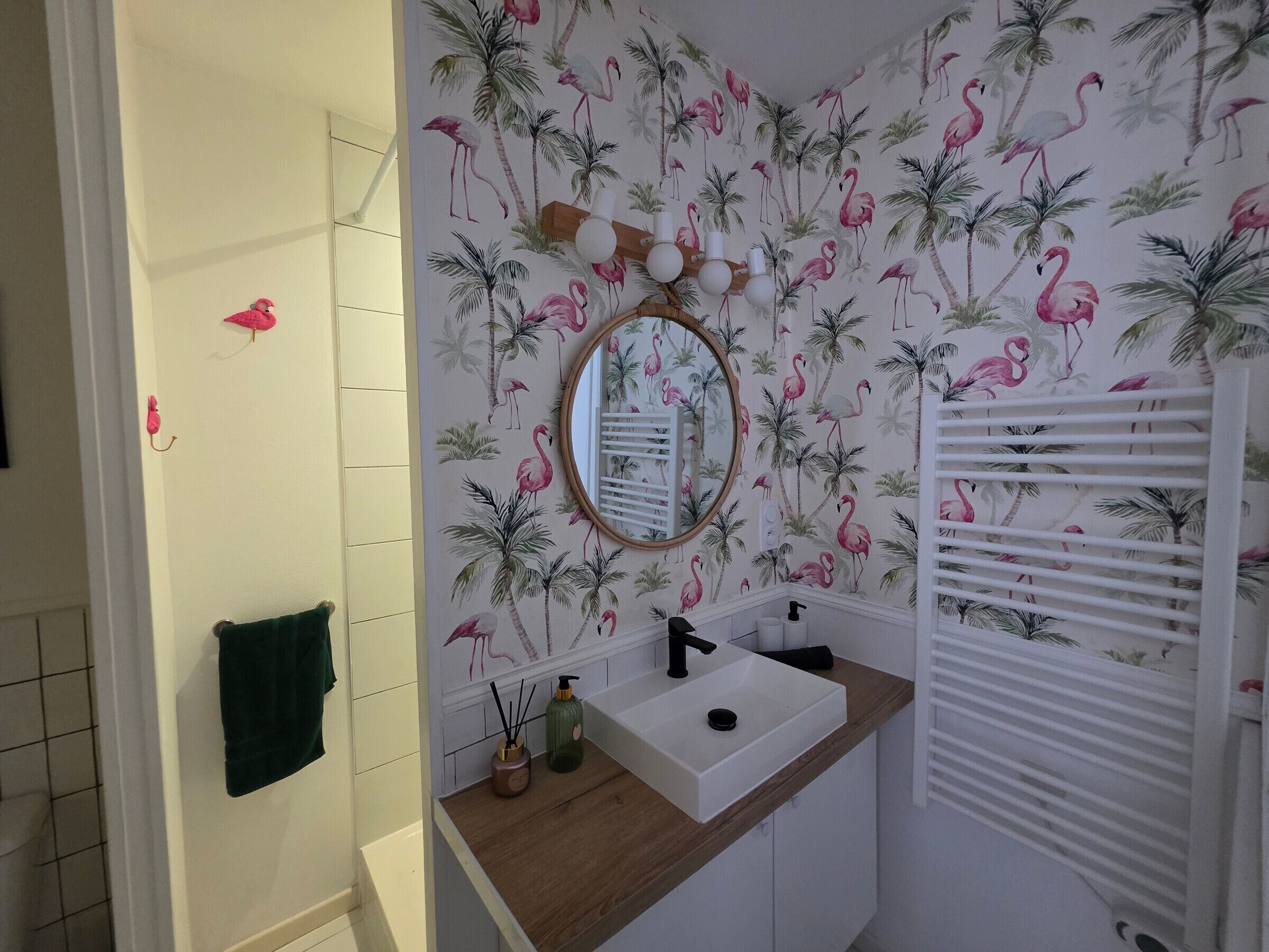 Un baño con un lavabo blanco, un espejo y un papel tapiz tropical con flamencos y palmeras.