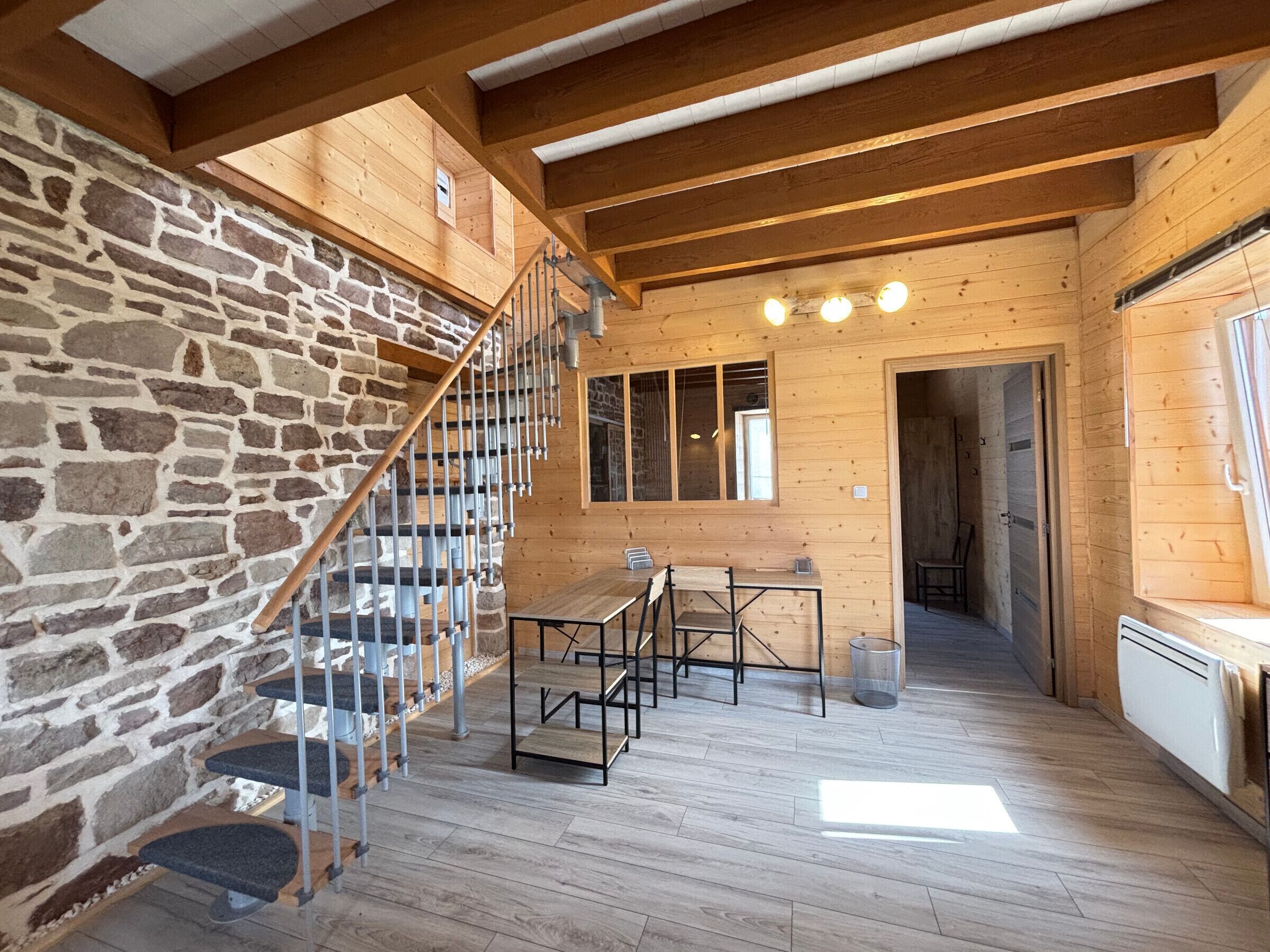 A wooden interior with a stone wall, a staircase, a dining area, and a kitchen.