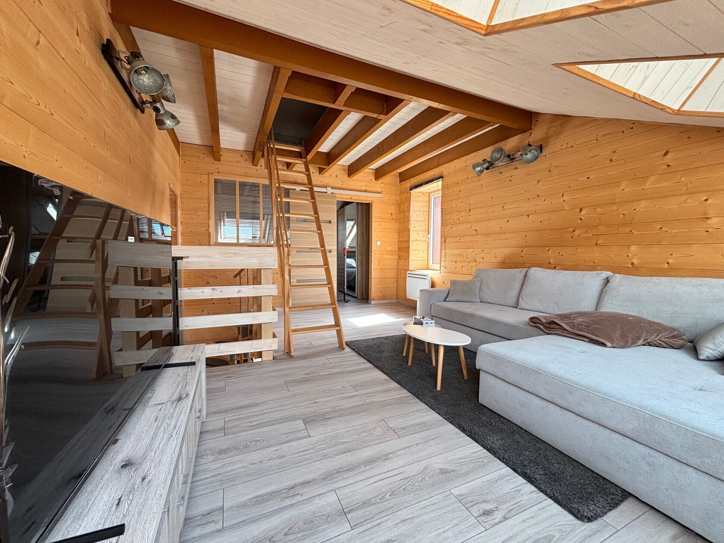 Interior de madera con zona de entrepiso, un sofá y una escalera.