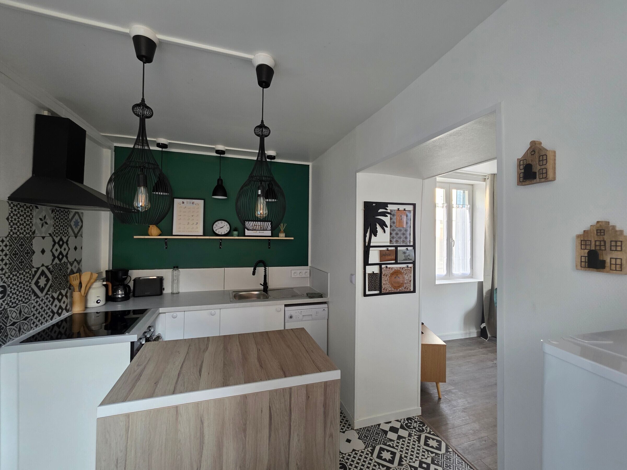 Une cuisine moderne avec un plan de travail en bois, des luminaires suspendus et un revêtement mural vert.