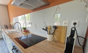 Una cocina moderna con tope de inducción negro, salpicadero de mármol blanco y armarios de madera.