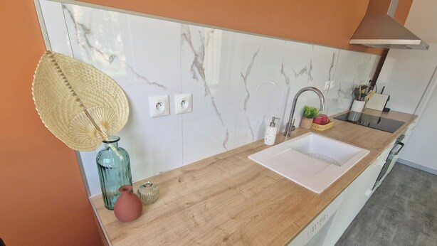 A kitchen with a wooden countertop, a sink, a faucet, and a backsplash with a marble pattern. - Renovated cottage near thermal baths (Luxeuil-les-Bains)