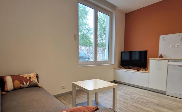 A living room with a sofa, a small table, a television, and a window with a view of the outside. - Renovated cottage near thermal baths (Luxeuil-les-Bains)