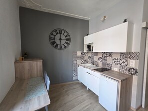Eine kompakte Küche mit Holztisch, weißen Schränken, einer schwarzen Uhr und Fliesen mit Muster.