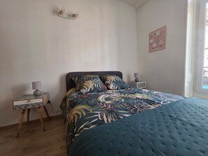 A bedroom with a bed, a nightstand, a lamp, and a wall decoration. - Cozy studio in the heart of Luxeuil - 1 guest (Luxeuil-les-Bains)