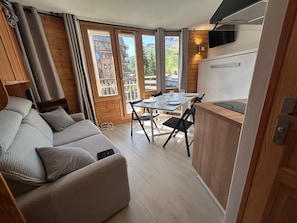A compact living space with a sofa, dining table, chairs, and a kitchenette. - Cozy apartment with balcony - 4 guests (Avoriaz)
