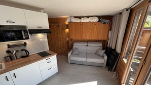 A compact living space with a kitchenette, a sofa, and a sliding door to a balcony. - Cozy apartment with balcony - 4 guests (Avoriaz)