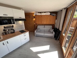 Ein kompakter Wohnraum mit Küchenzeile, einer Couch und einer Schiebetür zum Balkon.