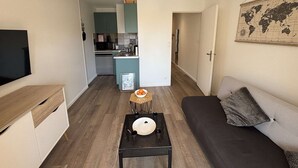 Ein gemütlicher, kleiner Wohnbereich mit einer Couch, einem Tisch mit Schüssel und Teller, einem Fernseher und einer Küchenzeile im Hintergrund.